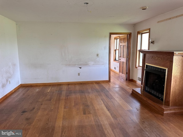 unfurnished living room featuring wood finished floors, a fireplace with raised hearth, and baseboards