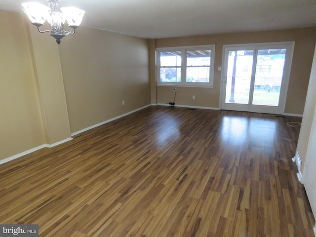 empty room with a chandelier, dark wood-style floors, and baseboards
