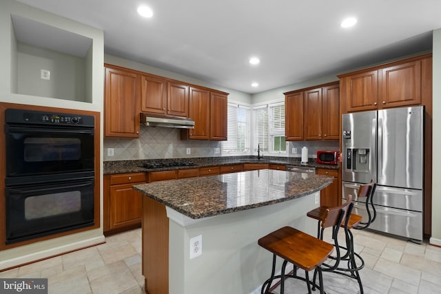 kitchen with black appliances, under cabinet range hood, backsplash, a kitchen breakfast bar, and a center island