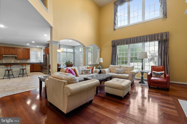 living room featuring ornate columns, arched walkways, a towering ceiling, hardwood / wood-style floors, and recessed lighting