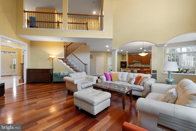 living room featuring decorative columns, arched walkways, light wood finished floors, a high ceiling, and stairway