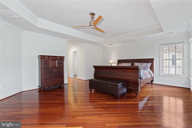 bedroom with a raised ceiling, wood finished floors, crown molding, and baseboards