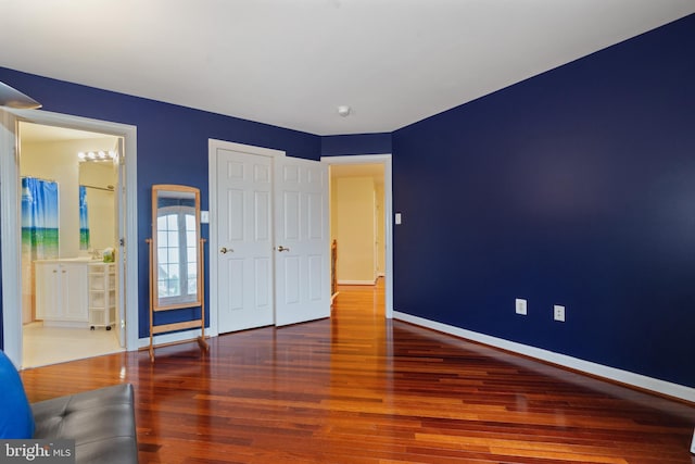 unfurnished bedroom featuring wood finished floors, baseboards, and ensuite bath