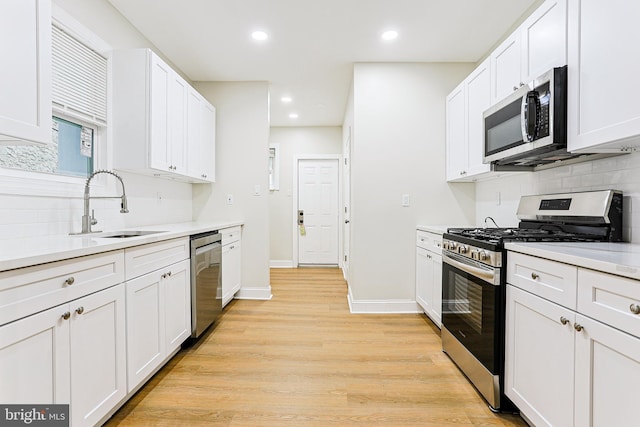 kitchen with appliances with stainless steel finishes, a sink, decorative backsplash, light wood finished floors, and light countertops