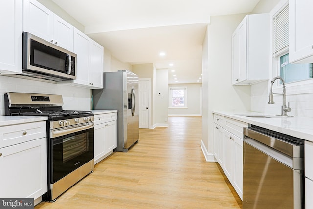 kitchen with stainless steel appliances, a sink, backsplash, light wood-style flooring, and white cabinets