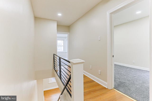 hallway with an upstairs landing, baseboards, light wood-style floors, and recessed lighting