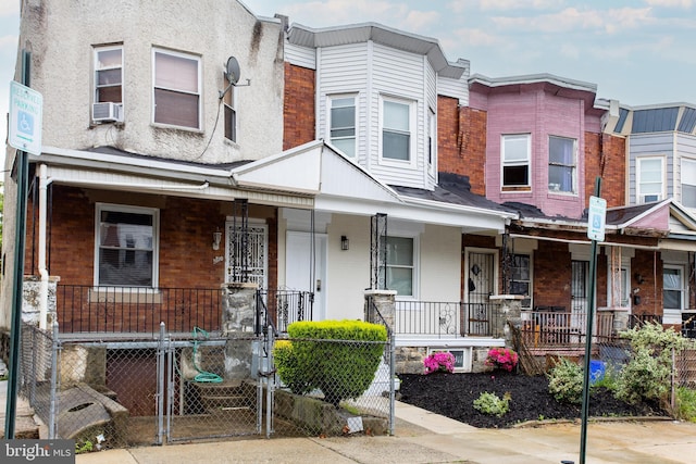 view of property with a porch, brick siding, a fenced front yard, a gate, and cooling unit