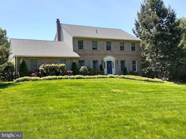 colonial-style house with brick siding, a front lawn, and a chimney