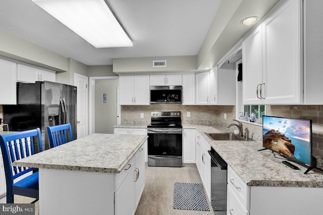 kitchen with stainless steel appliances, a sink, tasteful backsplash, a center island, and white cabinetry