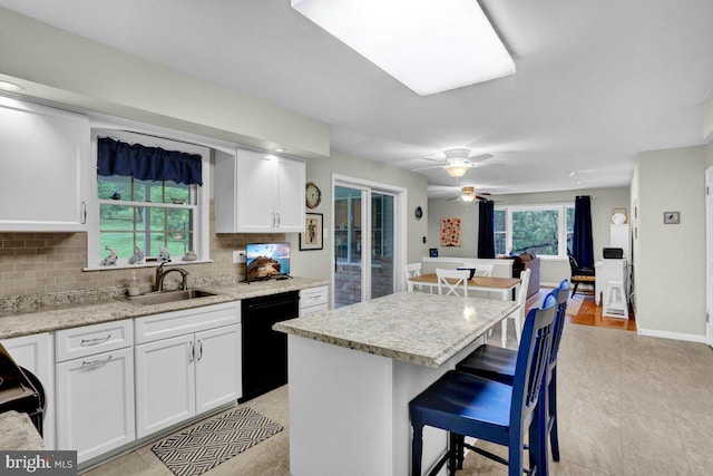 kitchen with a sink, dishwasher, decorative backsplash, white cabinets, and a kitchen bar