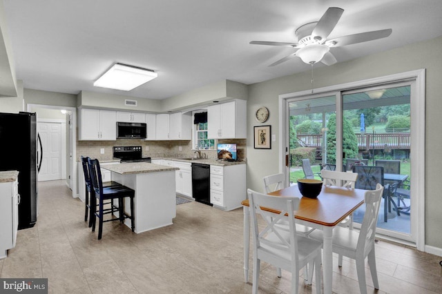 kitchen with black dishwasher, range with electric stovetop, freestanding refrigerator, a kitchen island, and white cabinetry