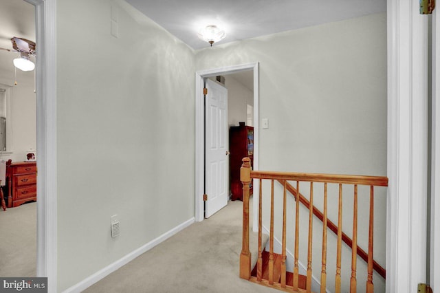hallway featuring carpet flooring, an upstairs landing, and baseboards
