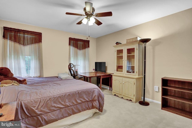 bedroom featuring light carpet, ceiling fan, baseboards, and a desk