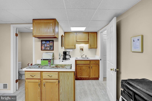 kitchen featuring a drop ceiling, light wood finished floors, a sink, light countertops, and baseboards