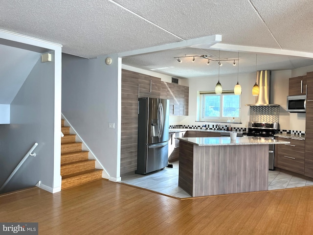 kitchen featuring appliances with stainless steel finishes, wall chimney exhaust hood, modern cabinets, a kitchen island, and light wood-style floors