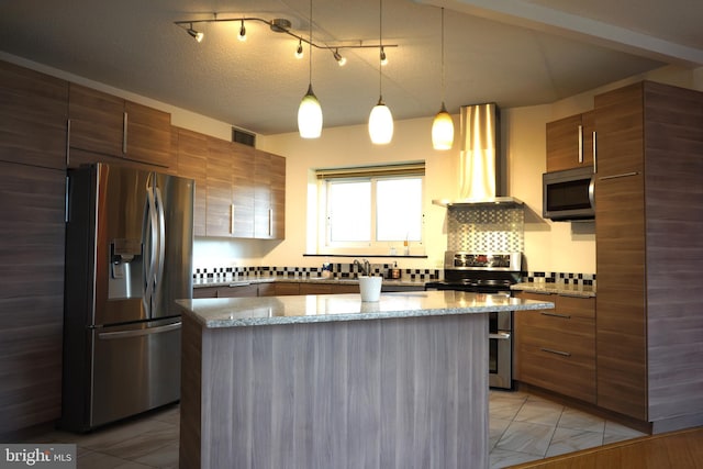 kitchen featuring stainless steel appliances, wall chimney range hood, a center island, tasteful backsplash, and brown cabinets