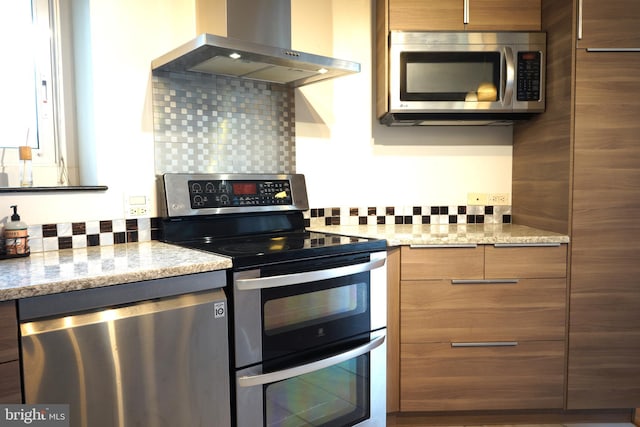 kitchen featuring stainless steel appliances, wall chimney range hood, modern cabinets, decorative backsplash, and brown cabinets