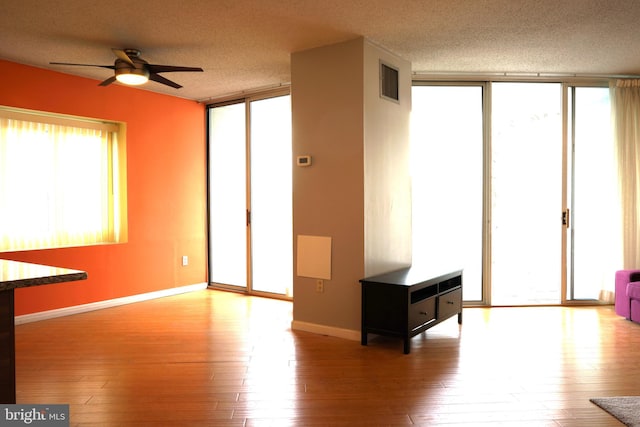 spare room with a wall of windows, a textured ceiling, ceiling fan, wood-type flooring, and baseboards