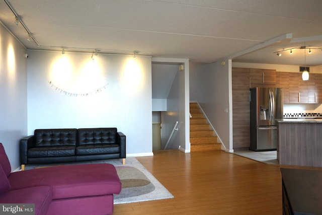 living room with rail lighting, light wood-type flooring, baseboards, and stairway