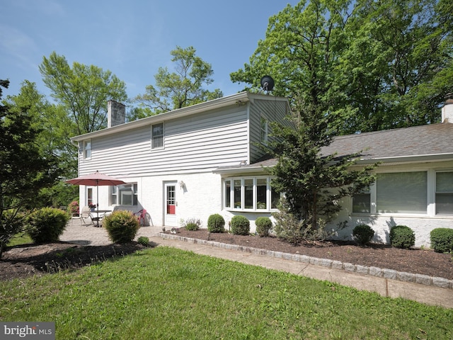view of front of property with a chimney, a patio, a front yard, and brick siding