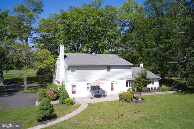 back of house with a chimney, a patio, and a lawn