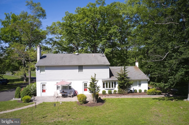 back of property with a chimney, a patio area, and a yard