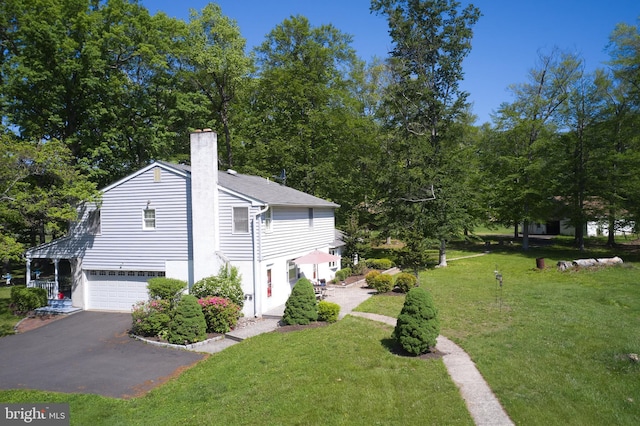 view of home's exterior with an attached garage, a chimney, asphalt driveway, and a lawn