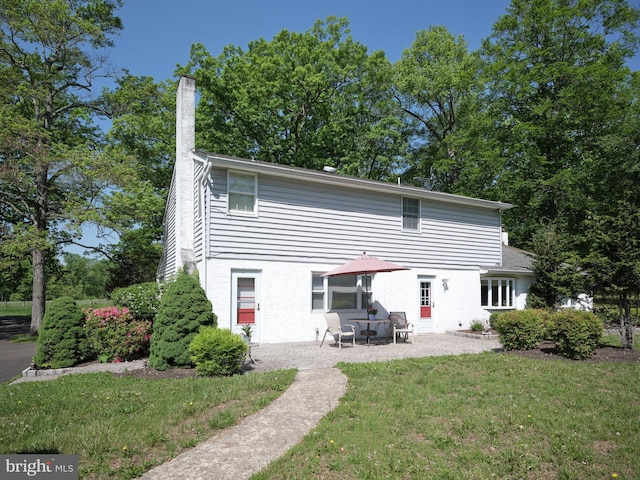 rear view of house with a chimney, a patio, a yard, and brick siding