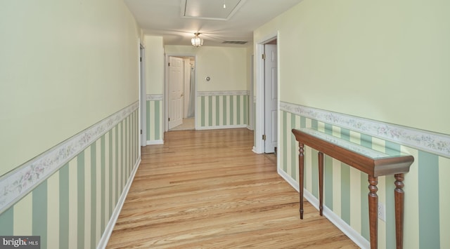 hallway with wallpapered walls, light wood-style floors, attic access, and wainscoting