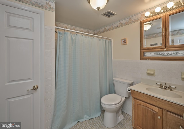 full bathroom with tile walls, tile patterned floors, toilet, vanity, and wainscoting