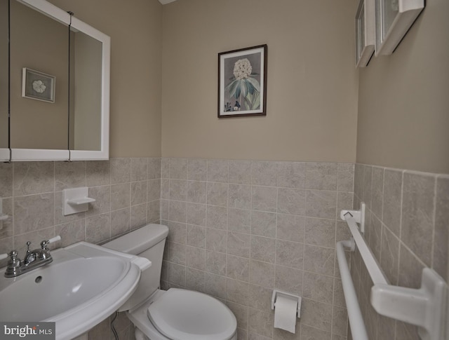 bathroom featuring tile walls, a sink, toilet, and a wainscoted wall