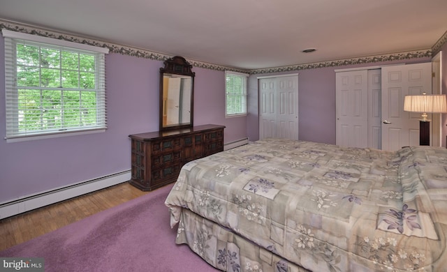 bedroom featuring two closets, wood finished floors, and baseboard heating