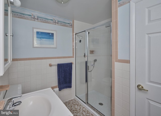 full bath with tile walls, a shower stall, a sink, and wainscoting