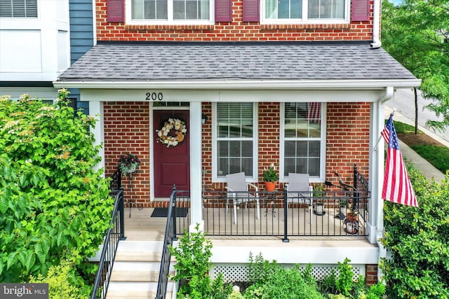 view of exterior entry featuring roof with shingles and brick siding