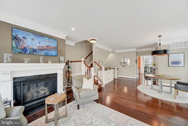 living area with wood finished floors, ornamental molding, stairs, baseboards, and a glass covered fireplace