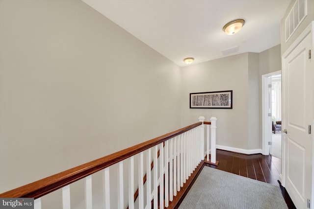 corridor with dark wood-style floors, an upstairs landing, and baseboards