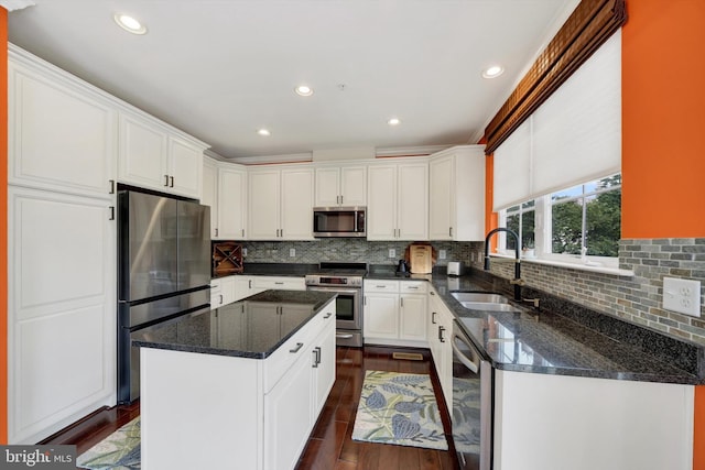 kitchen featuring appliances with stainless steel finishes, a sink, white cabinetry, dark wood finished floors, and a center island