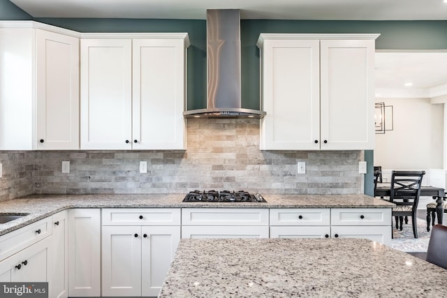 kitchen with wall chimney exhaust hood, black gas cooktop, white cabinets, tasteful backsplash, and light stone countertops