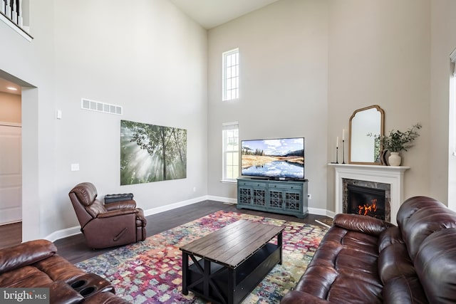 living room featuring a towering ceiling, wood finished floors, baseboards, and a high end fireplace