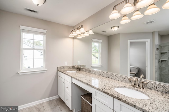 bathroom with baseboards, toilet, double vanity, tiled shower, and tile patterned floors