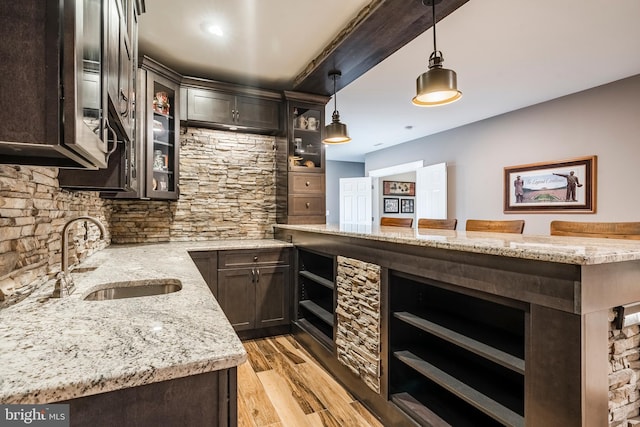 kitchen featuring a sink, dark brown cabinets, light wood finished floors, light stone counters, and pendant lighting