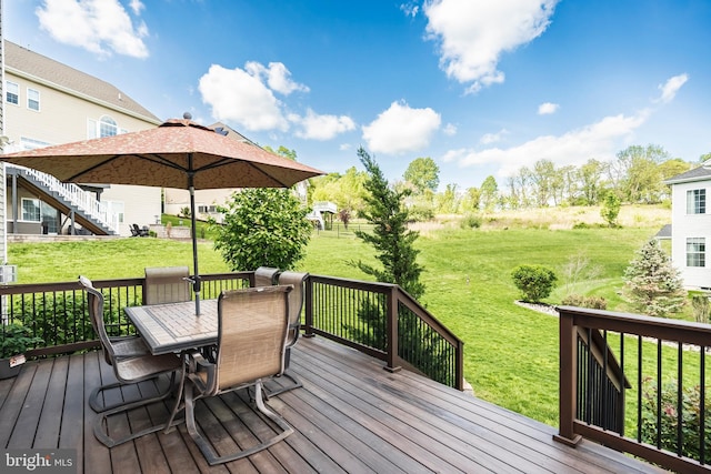 wooden terrace featuring outdoor dining space and a lawn
