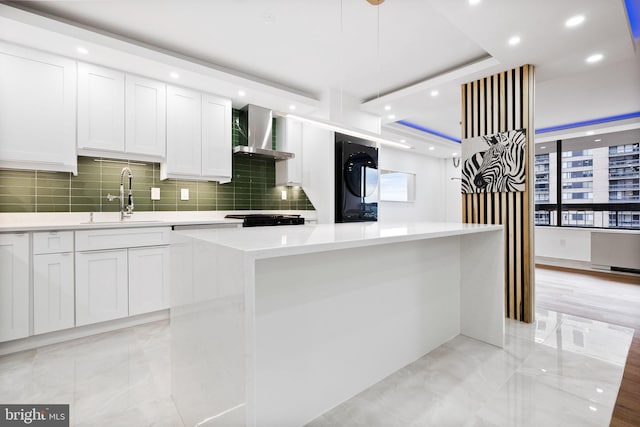 kitchen with a sink, wall chimney range hood, tasteful backsplash, white cabinets, and stacked washer and clothes dryer
