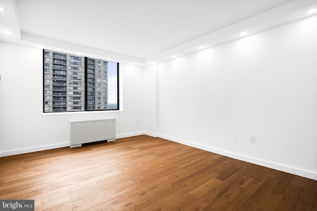 empty room with recessed lighting, radiator, wood finished floors, and baseboards
