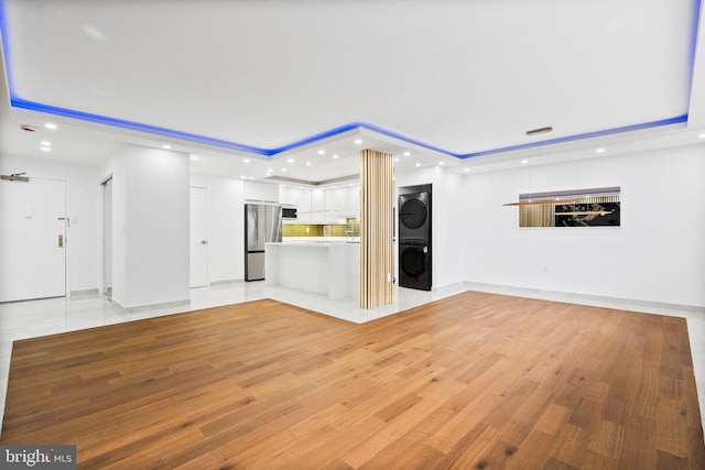unfurnished living room with estacked washer and dryer, a tray ceiling, recessed lighting, and light wood-type flooring