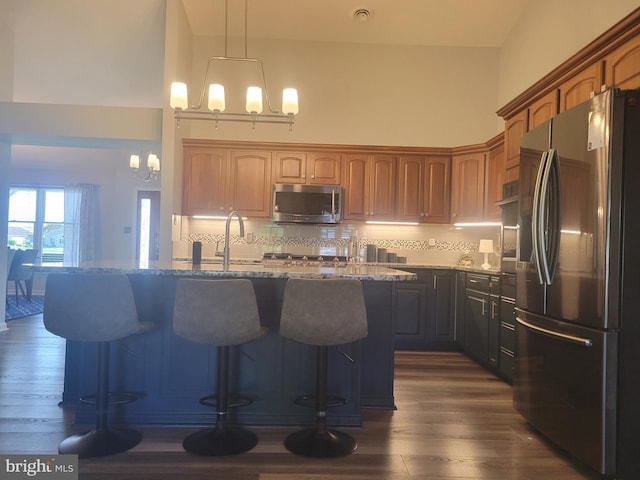 kitchen with appliances with stainless steel finishes, light stone counters, a chandelier, dark wood-type flooring, and a breakfast bar
