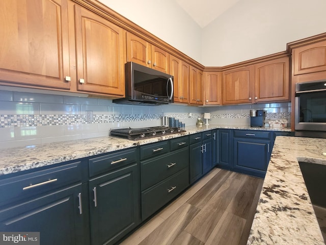 kitchen with appliances with stainless steel finishes, tasteful backsplash, light stone counters, vaulted ceiling, and wood finished floors