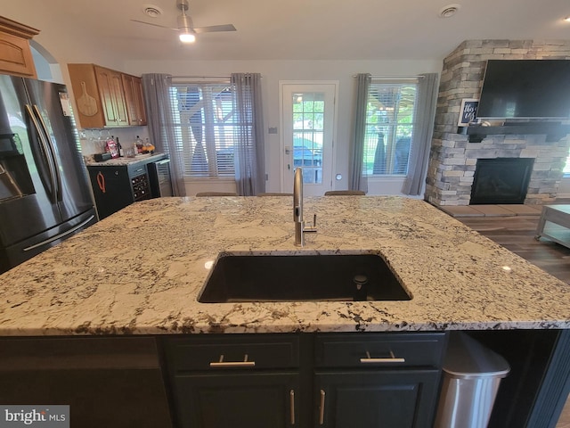 kitchen featuring a sink, freestanding refrigerator, open floor plan, a stone fireplace, and plenty of natural light