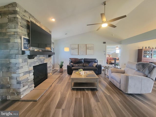 living room featuring a ceiling fan, wood finished floors, vaulted ceiling, and a stone fireplace