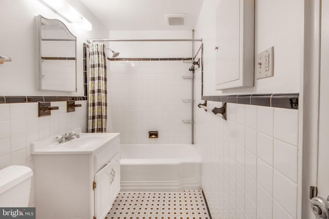 bathroom featuring tile walls, toilet, shower / bath combo with shower curtain, and vanity